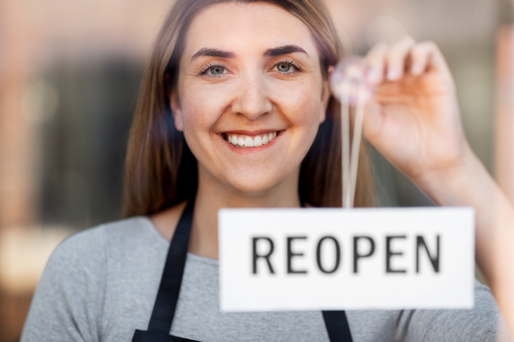 small business, reopening and service concept - happy smiling woman hanging reopen banner to window or door glass. happy woman hanging reopen banner to door glass