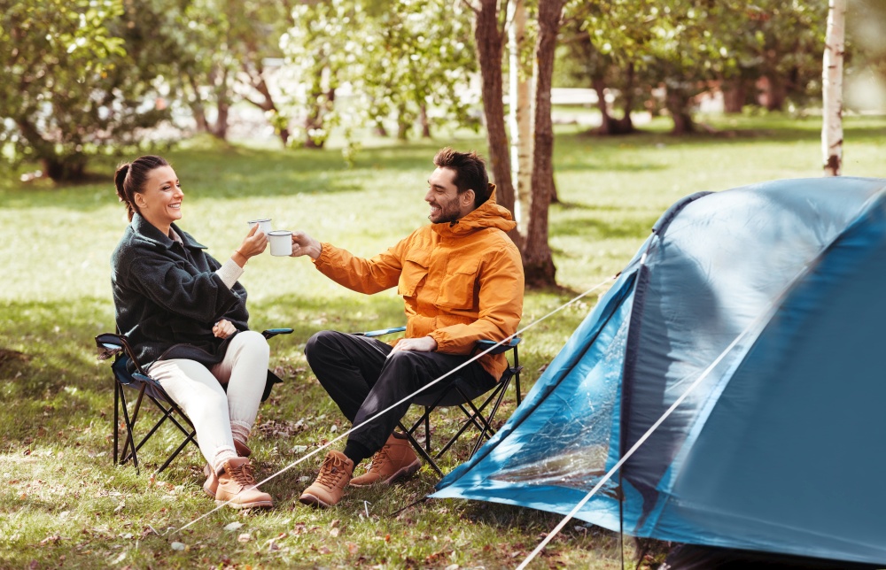 camping, tourism and travel concept - happy couple drinking tea at tent camp. happy couple drinking tea at tent camp