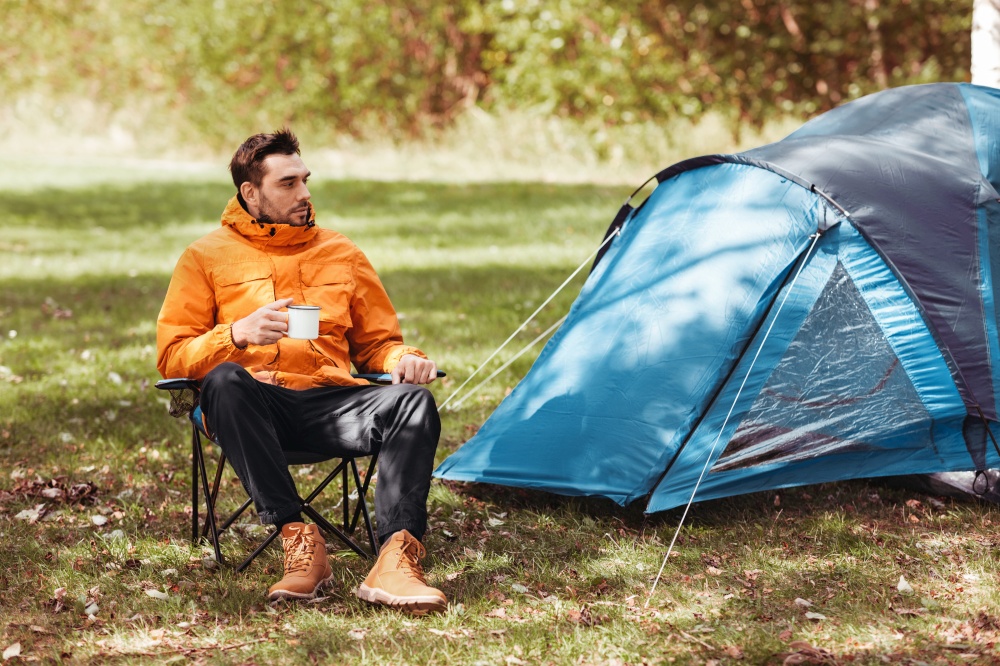 camping, tourism and travel concept - happy man drinking tea at tent camp. happy man drinking tea at tent camp