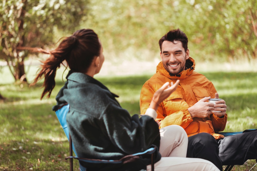 camping, tourism and travel concept - happy couple drinking tea at campsite. happy couple drinking tea at tent campsite