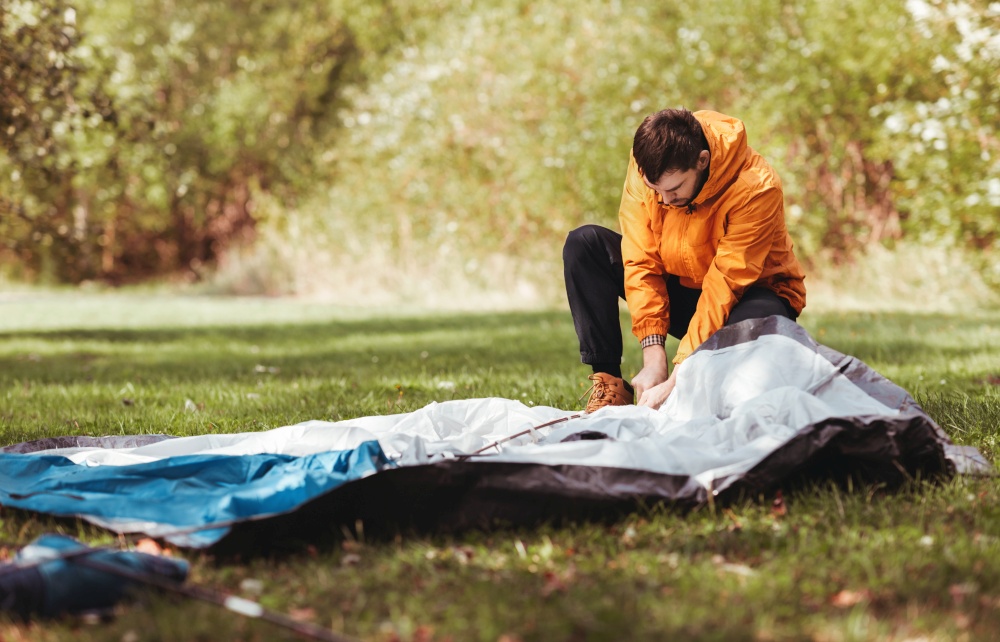 camping, tourism and concept - man setting up tent outdoors. man setting up tent outdoors