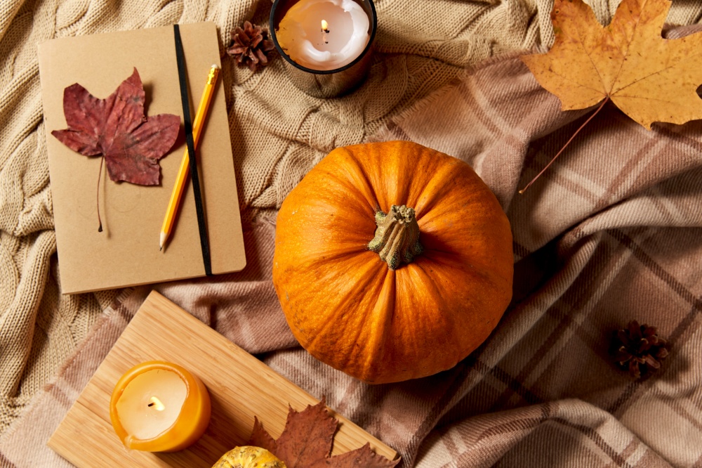 autumn, season and leisure concept - notebook or diary with pencil, pumpkins and candle on warm blankets at home. pumpkins, diary, pencil, autumn leaves and candles
