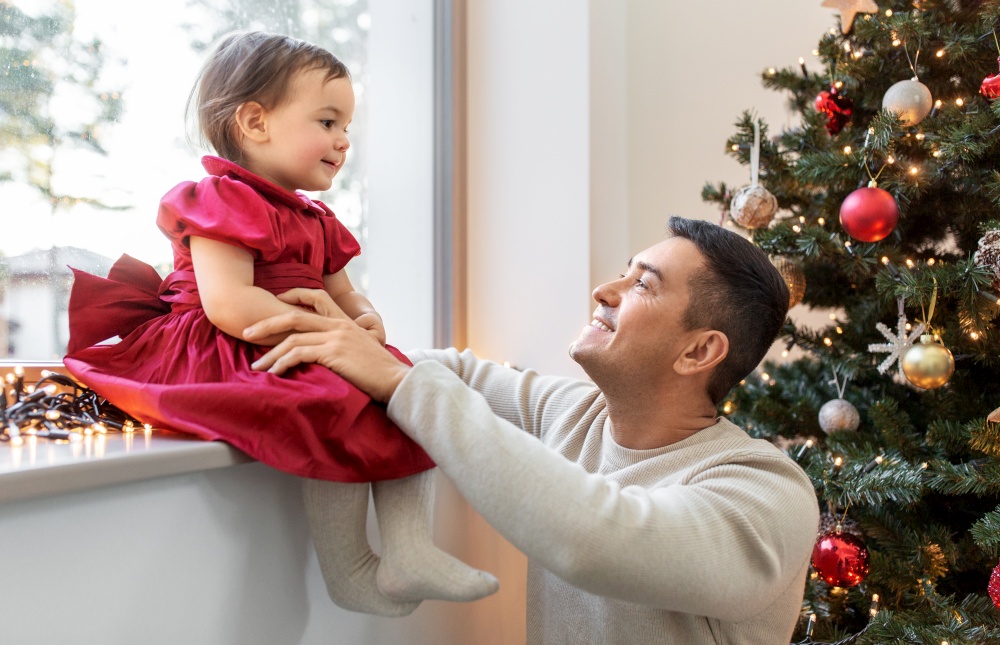 winter holidays and family concept - happy middle-aged father and baby daughter over christmas tree at home. happy father and baby girl over christmas tree