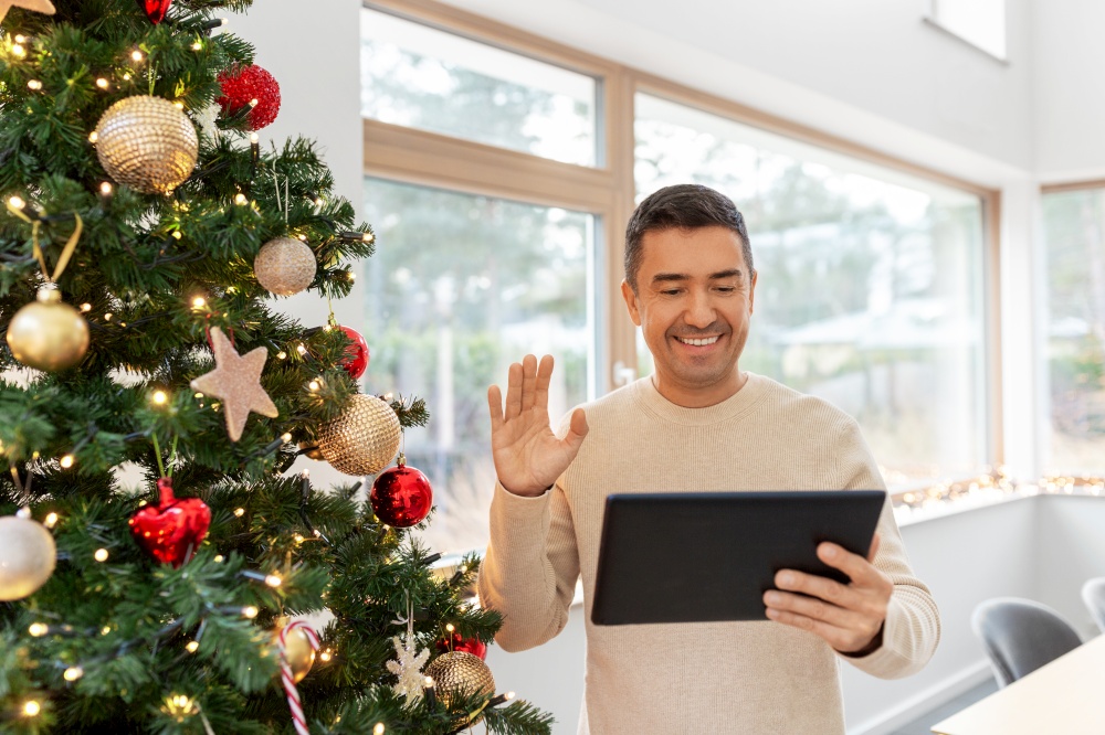 people and holidays concept - happy smiling middle aged man with tablet pc computer having video call at home. man with tablet pc having video call on christmas