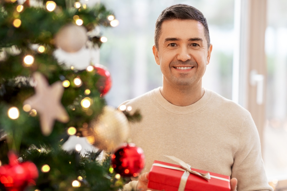 christmas, people and holidays concept - happy smiling middle aged man with gift box at home. happy middle aged man with christmas gift at home