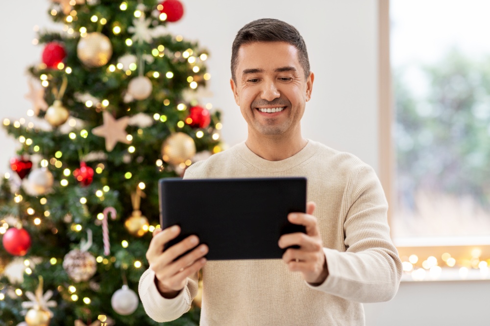 people and holidays concept - happy smiling middle aged man with tablet pc computer at home. happy middle aged man with tablet pc on christmas