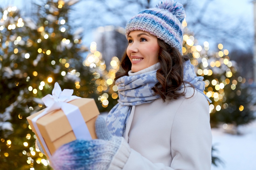 christmas, holidays and people concept - happy smiling young woman with gift box in winter park. happy young woman with christmas gift in winter