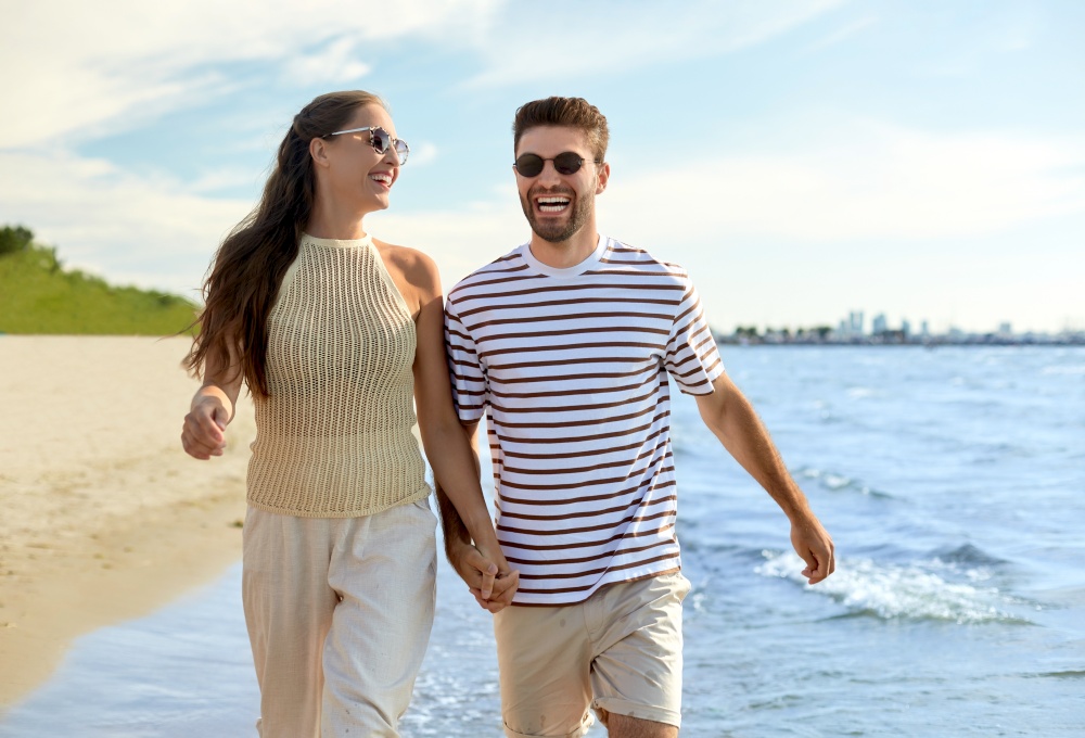 leisure, relationships and people concept - happy couple in sunglasses walking in water along summer beach. happy couple walking in water along summer beach