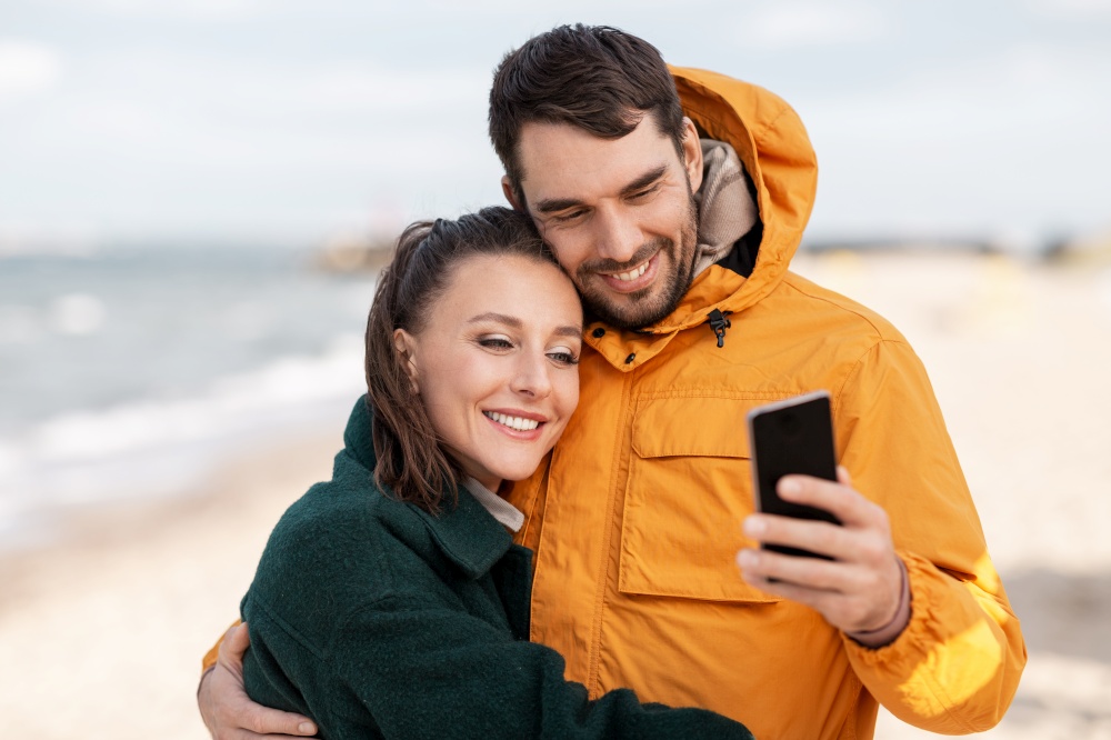 technology, relationships and people concept - happy couple with smartphone on autumn beach. couple with smartphone on autumn beach