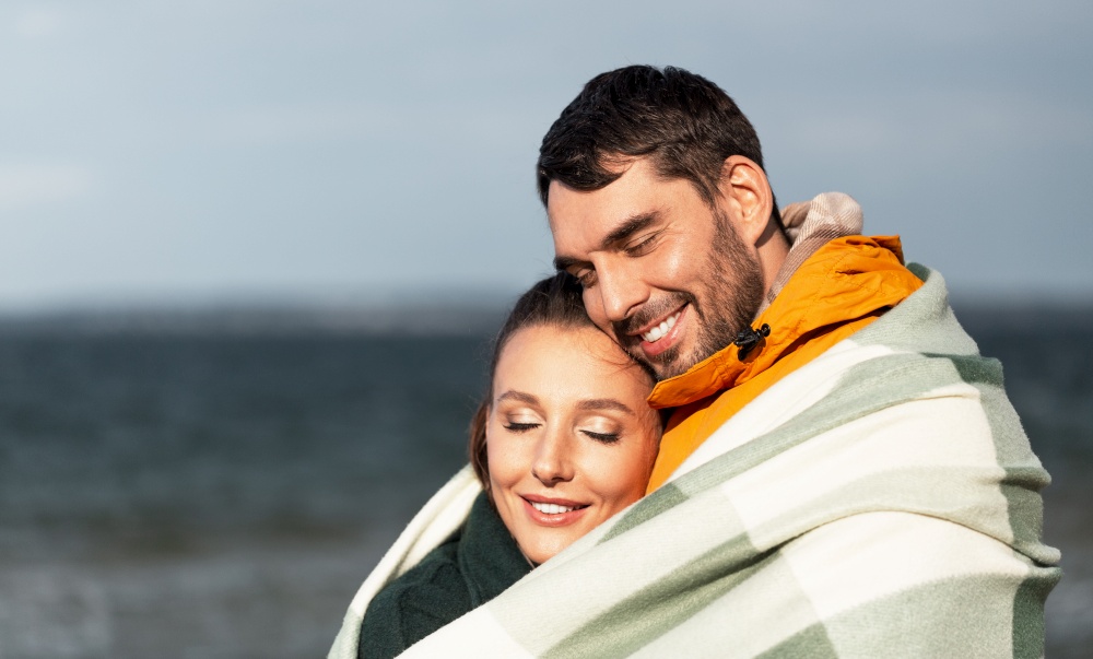 love, relationship and people concept - happy smiling couple in warm blanket on autumn beach. happy couple in warm blanket on autumn beach