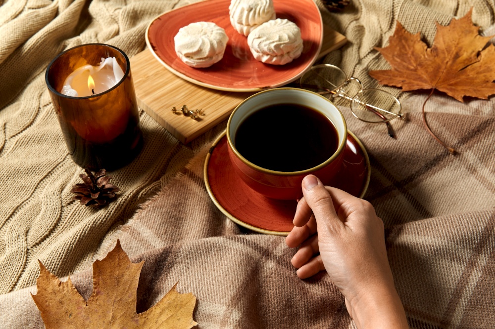 people, season and leisure concept - cup of coffee, autumn leaves, meringues and candle on warm blankets at home. cup of coffee, autumn leaves and candle in bed