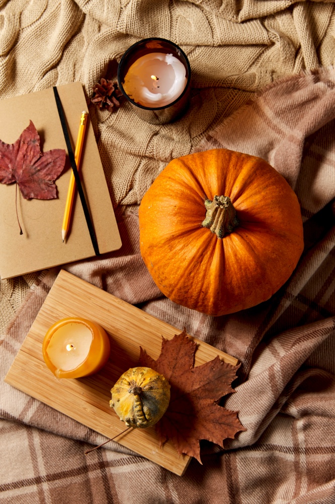 autumn, season and leisure concept - notebook or diary with pencil, pumpkins and candle on warm blankets at home. pumpkins, diary, pencil, autumn leaves and candles