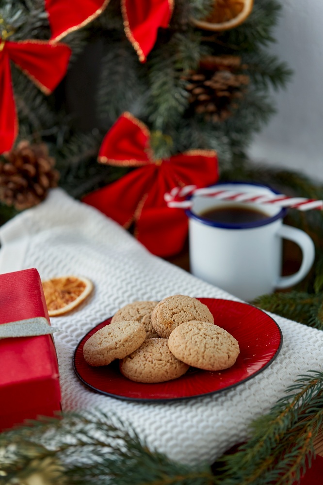 bake, food and winter holidays concept - oatmeal cookies on red ceramic plate and christmas decorations at home. cookies on plate and christmas decorations at home