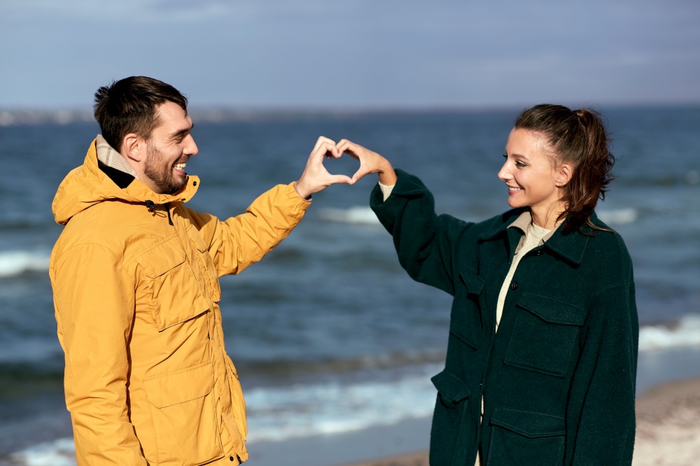 love, relationship and people concept - happy couple making hand heart gesture on autumn beach. happy couple making hand heart on autumn beach