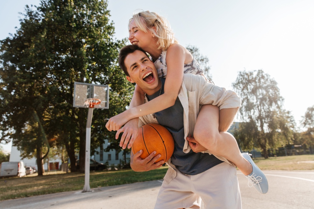 summer holidays, love and people concept - happy young couple with ball having fun on basketball playground. happy couple having fun on basketball playground