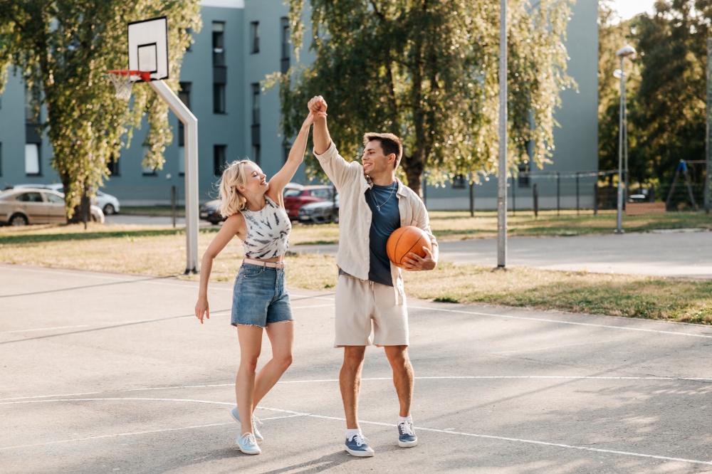 sport, love and people concept - happy young couple with ball holding hands on basketball playground. happy couple with ball on basketball playground