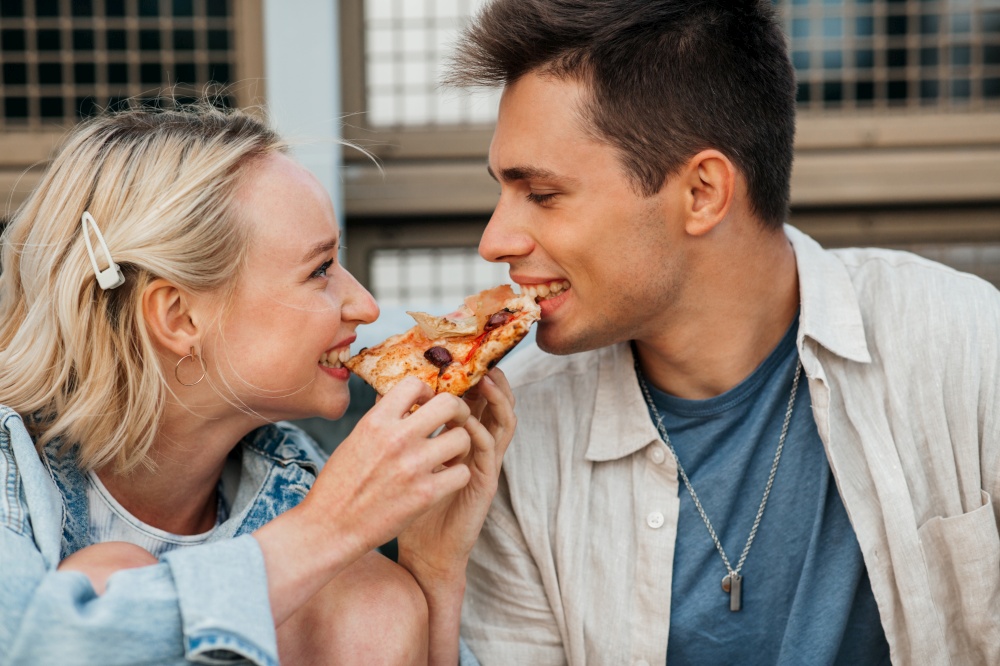 food and people concept - happy young couple eating takeaway pizza outdoors. happy couple eating pizza outdoors