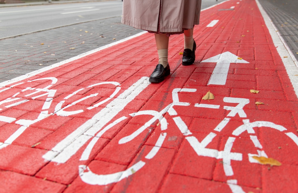 city and traffic concept - close up of woman&rsquo;s feet walking along separate bike lane or red road with signs only for bicycles on street. feet walking along bike lane or road for bicycles