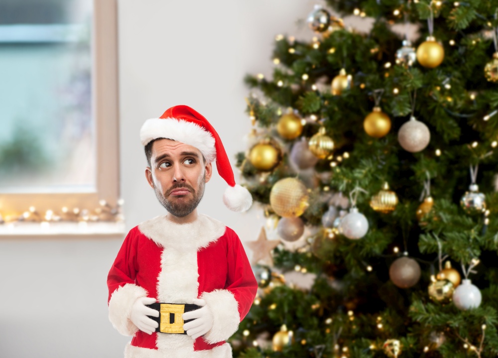 emotion, expression and winter holiday concept - sad man in santa claus costume over christmas tree on home background (funny cartoon style character with big head). sad man in santa claus costume over christmas tree