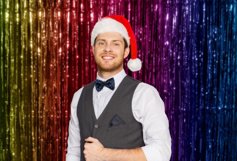 celebration, people and winter holidays concept - happy man in santa hat and suit at christmas party over foil fringe on background. happy man in santa hat and suit on christmas
