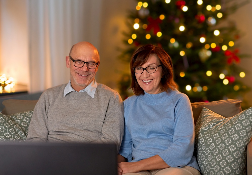 winter holidays, leisure and people concept - happy smiling senior couple watching tv at home in evening over christmas tree lights on background. happy senior couple watching tv on christmas