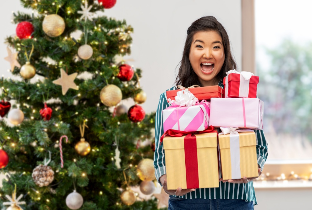 winter holidays and people concept - happy asian young woman with gift box over christmas tree on background. happy asian woman with birthday present