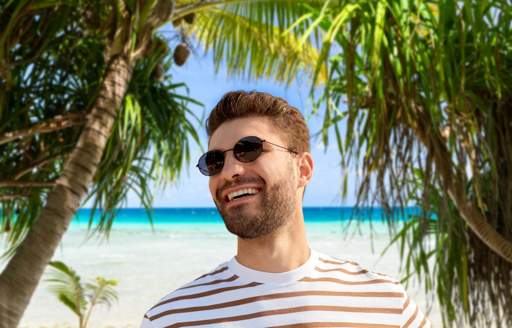 travel, tourism and people concept - portrait of young man in sunglasses over tropical beach background in french polynesia. young man in sunglasses over exotic beach
