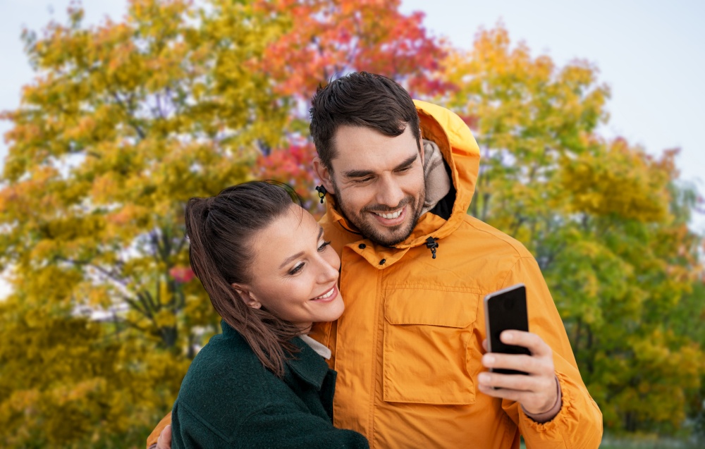 technology, season and people concept - happy couple with smartphone over autumn park background. couple with smartphone over autumn park background