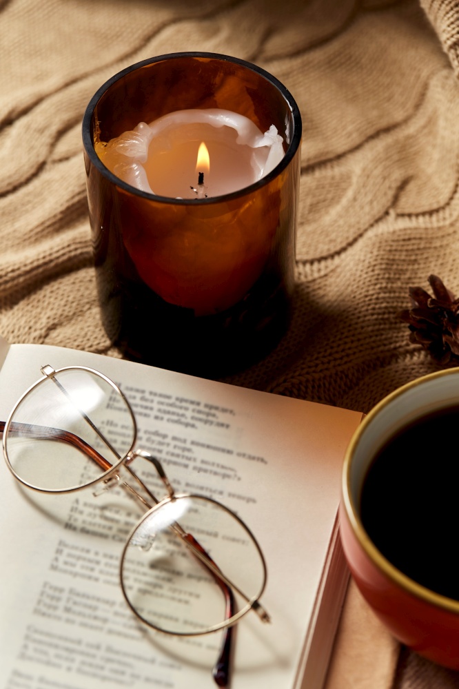 hygge, season and leisure concept - close up of open book of poems with glasses, cup of coffee and candle in holder burning on warm blanket at home. book, glasses, coffee and candle on warm blanket