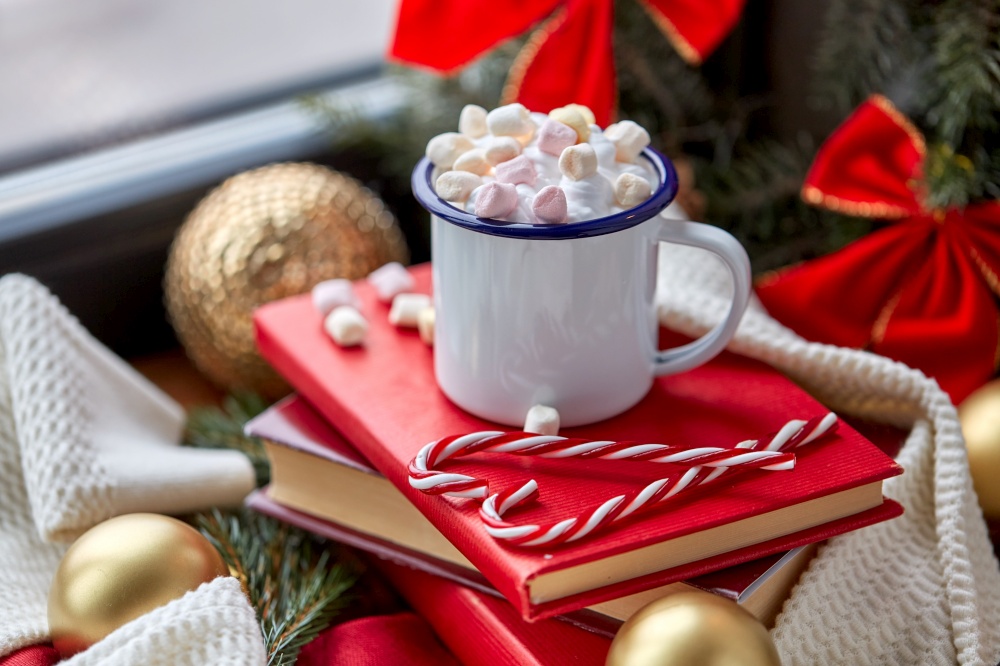 holidays, christmas and celebration concept - camp mug of whipped cream with marshmallow, candy canes, books and decorations at home. cup of whipped cream with marshmallow on christmas