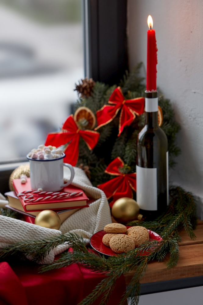 christmas and holidays concept - cup of whipped cream with marshmallow, candy canes, books, oatmeal cookies and decorations at home. christmas treats and decorations on sill