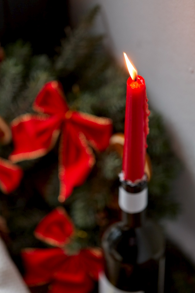 christmas, holidays and objects concept - close up of red candle burning in candlestick made of wine bottle at home. red christmas candle burning in wine bottle