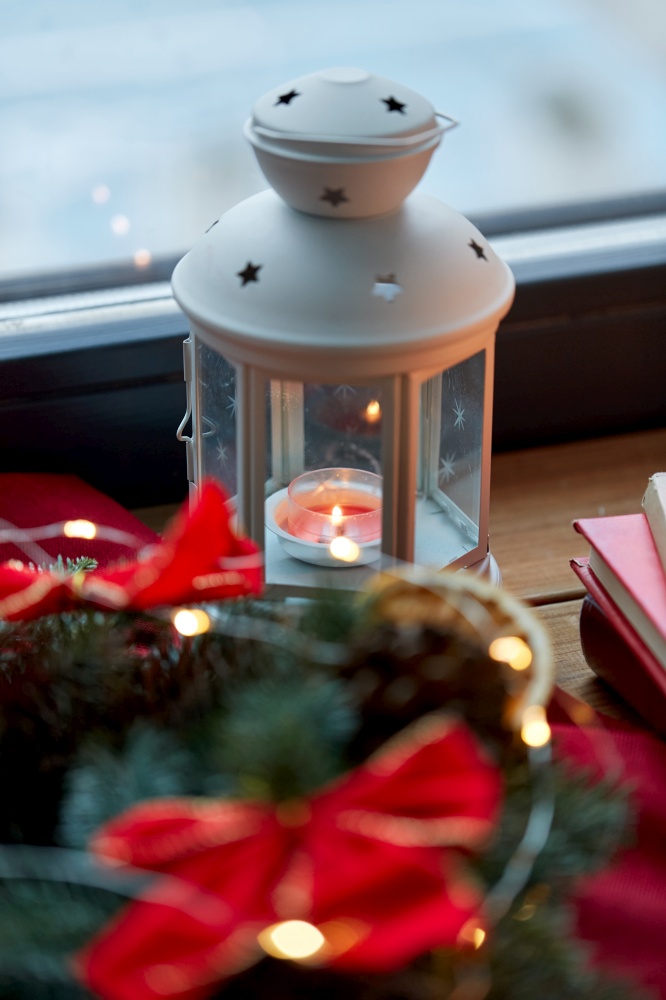 winter holidays, new year and decorations concept - close up of candle burning in christmas lantern on window sill at home. candle burning in christmas lantern on window sill