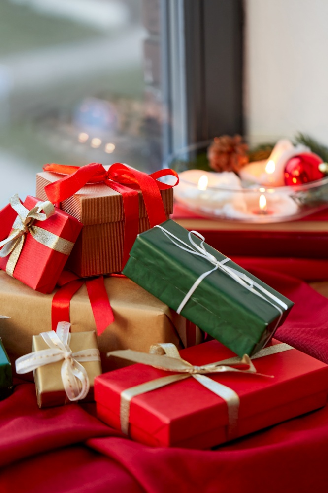 holidays, new year and celebration concept - heap of christmas gifts on red tablecloth on window sill. christmas gifts on red tablecloth on window sill