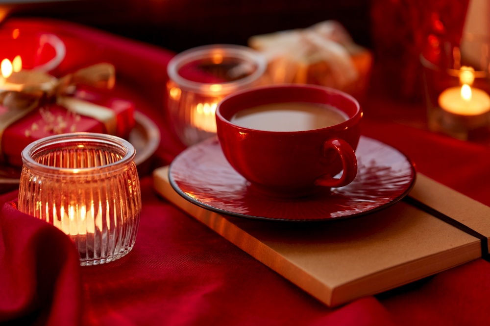 holidays, christmas and celebration concept - coffee in red ceramic cup with saucer and burning candles at home. cup of coffee and candles at home on christmas