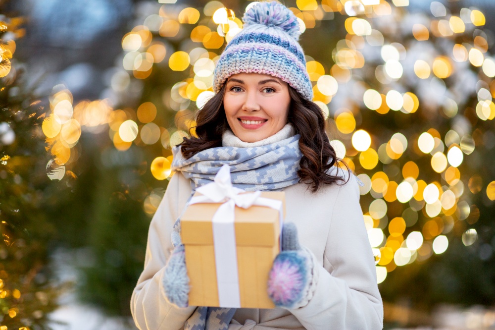 winter holidays, celebration and people concept - happy smiling woman with christmas gift over festive lights. happy woman with christmas gift over lights