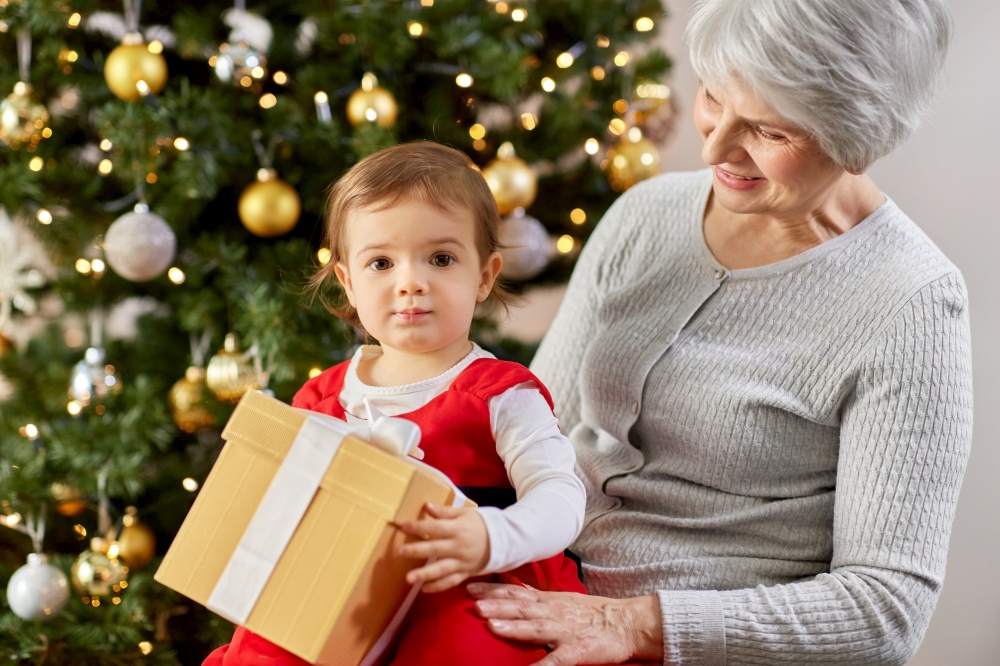christmas, holidays and family concept - happy grandmother and baby granddaughter with gift at home. grandmother and baby girl with christmas gift