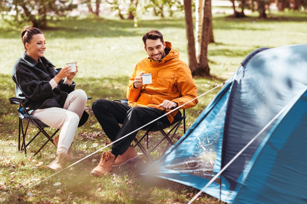 camping, tourism and travel concept - happy couple drinking tea at tent camp. happy couple drinking tea at tent camp