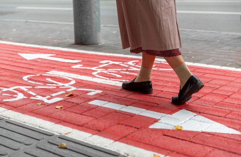 city and traffic concept - close up of woman&rsquo;s feet walking along separate bike lane or red road with signs only for bicycles on street. feet walking along bike lane or road for bicycles
