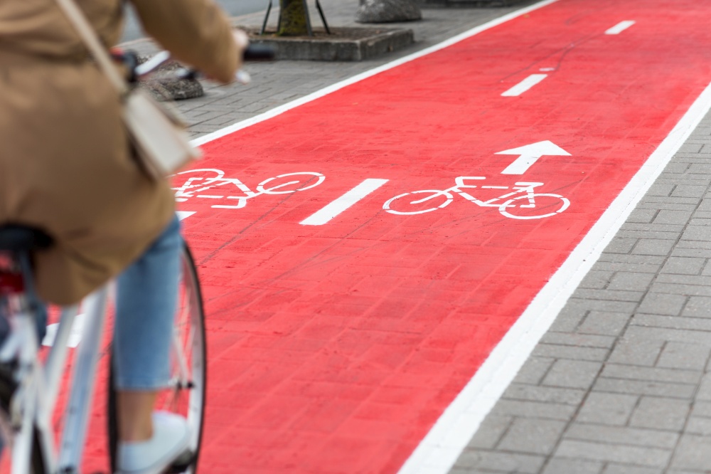 traffic, city transport and people concept - woman cycling along red bike lane with signs of bicycles on street. woman cycling along red bike lane road in city
