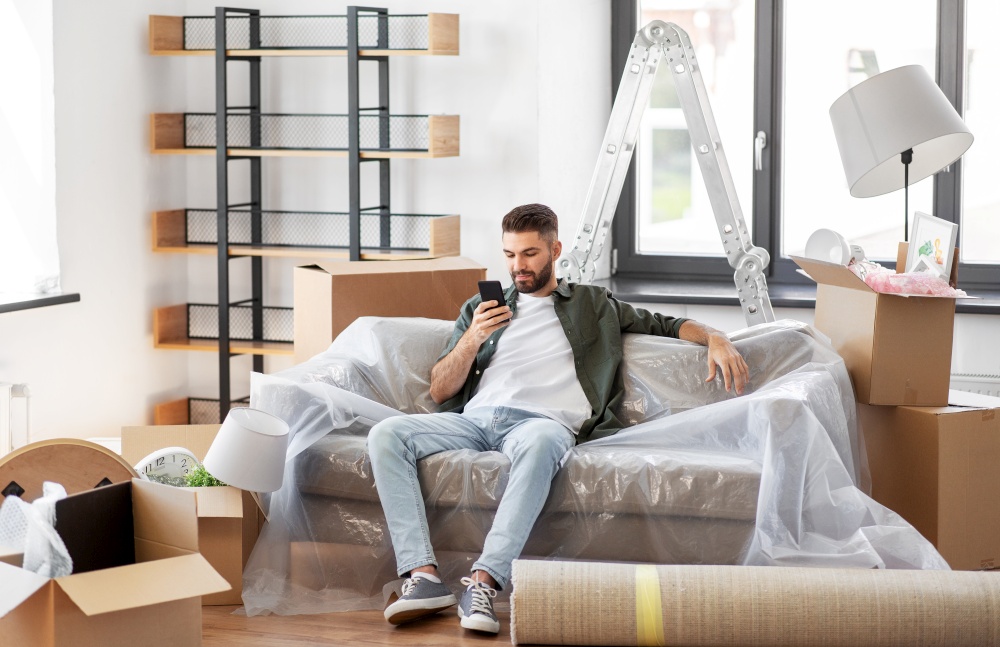 moving, people and real estate concept - man with smartphone and boxes at new home. man with smartphone and boxes moving into new home