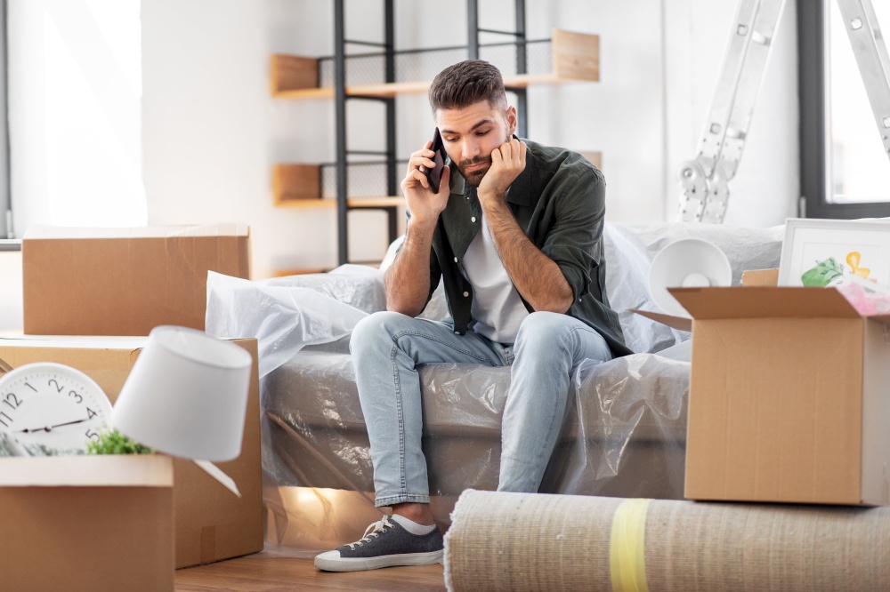 moving, people and real estate concept - sad man with boxes calling on smartphone at new home. sad man calling on smartphone moving to new home