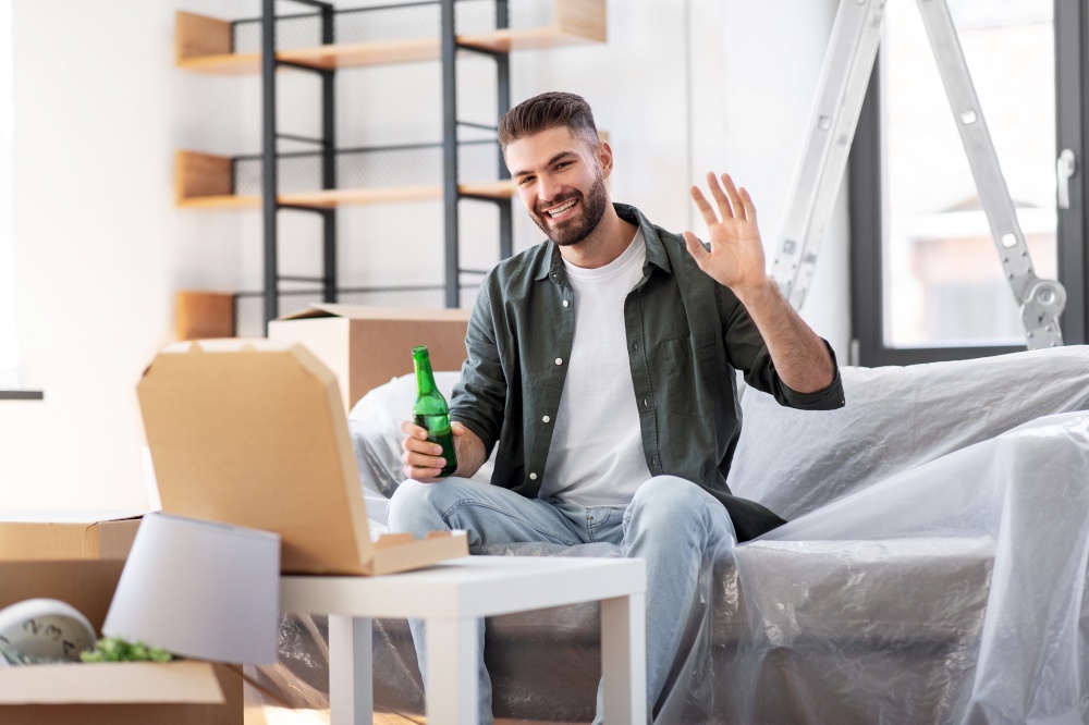moving, people and real estate concept - happy smiling man with box of pizza and beer bottle at new home waving hand. man with box of pizza and beer bottle at new home