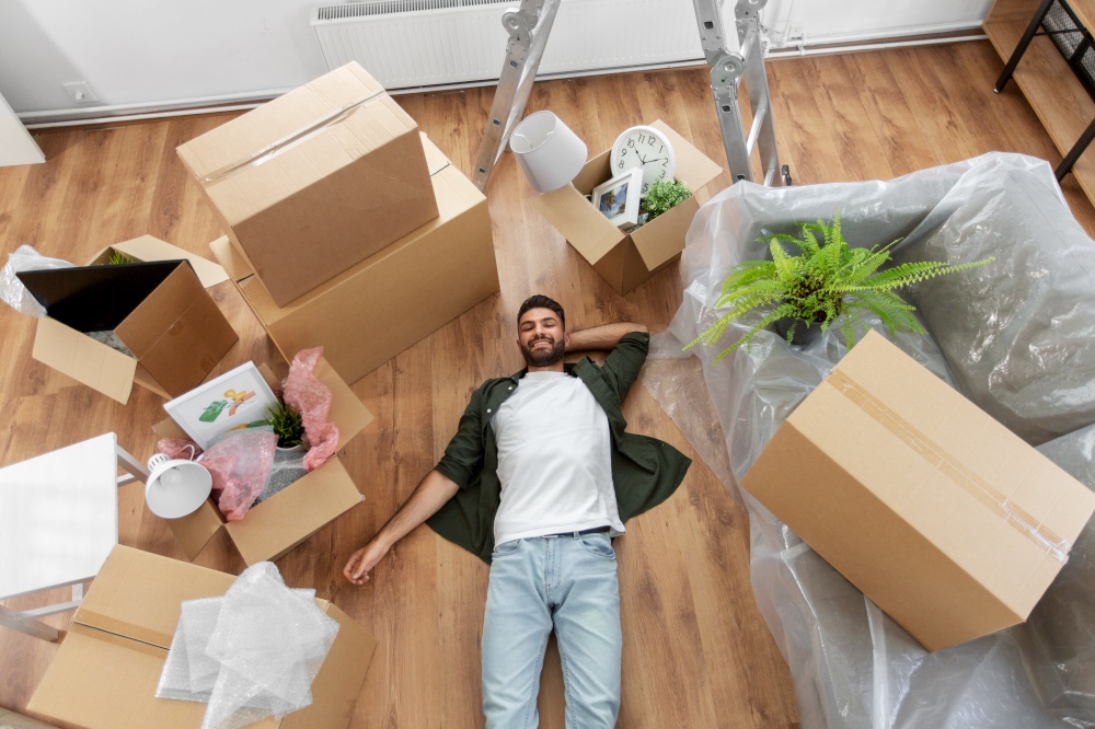 moving, people and real estate concept - happy smiling man with boxes lying on floor at new home. happy man with boxes moving to new home