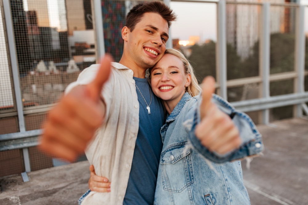 summer holidays, love and people concept - happy young couple hugging and showing thumbs up on roof top city parking. happy young couple showing thumbs up on roof top