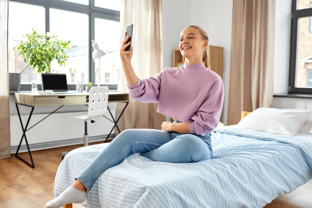 people, children and technology concept - happy smiling teenage girl with smartphone taking selfie at home. happy girl with smartphone taking selfie at home