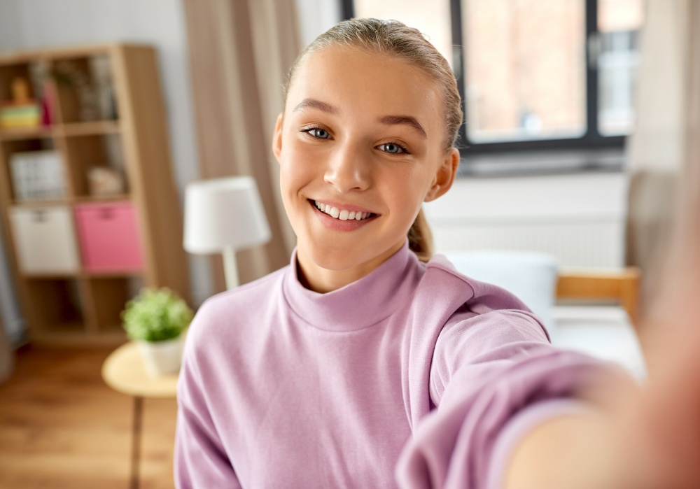 people, children and technology concept - happy smiling girl taking selfie at home. happy smiling girl taking selfie at home