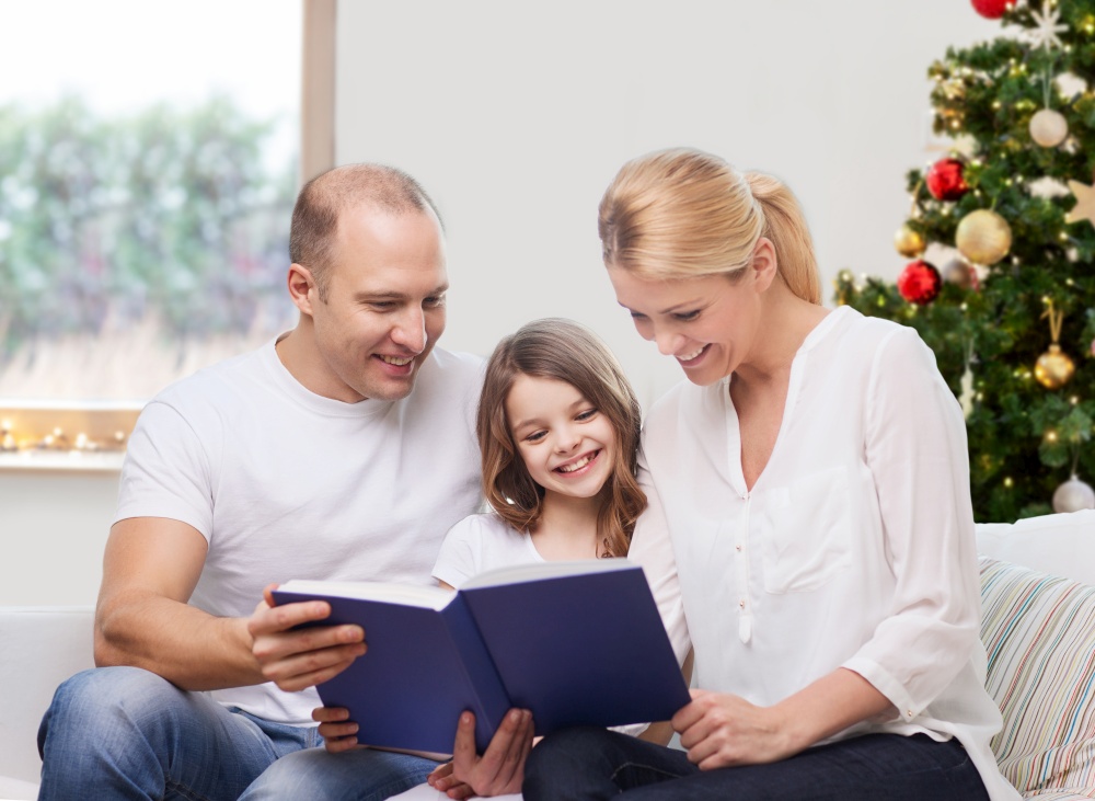 family, winter holidays and technology concept - happy mother, father and daughter sitting on sofa and reading book at home over christmas tree lights background. happy family reading book at home on christmas