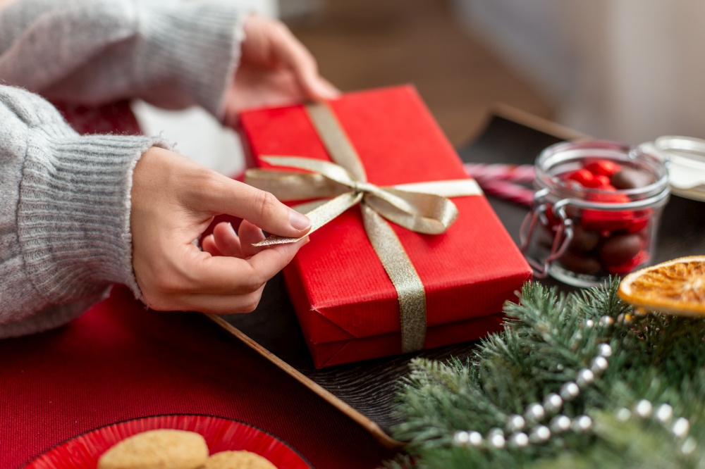 winter holidays and celebration concept - hands with christmas gift, treats and decorations on table at home. hands with christmas gift, treats and decorations