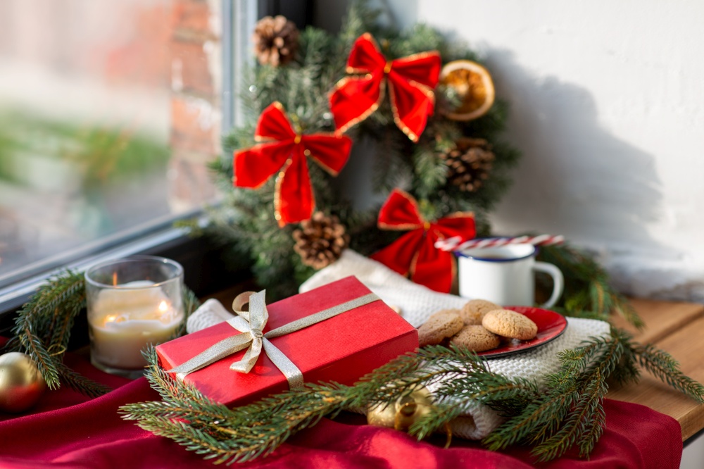 winter holidays, decoration and celebration concept - christmas gift, cookies, candle and fir branch on window sill at home. christmas gift, cookies, candle and fir branch